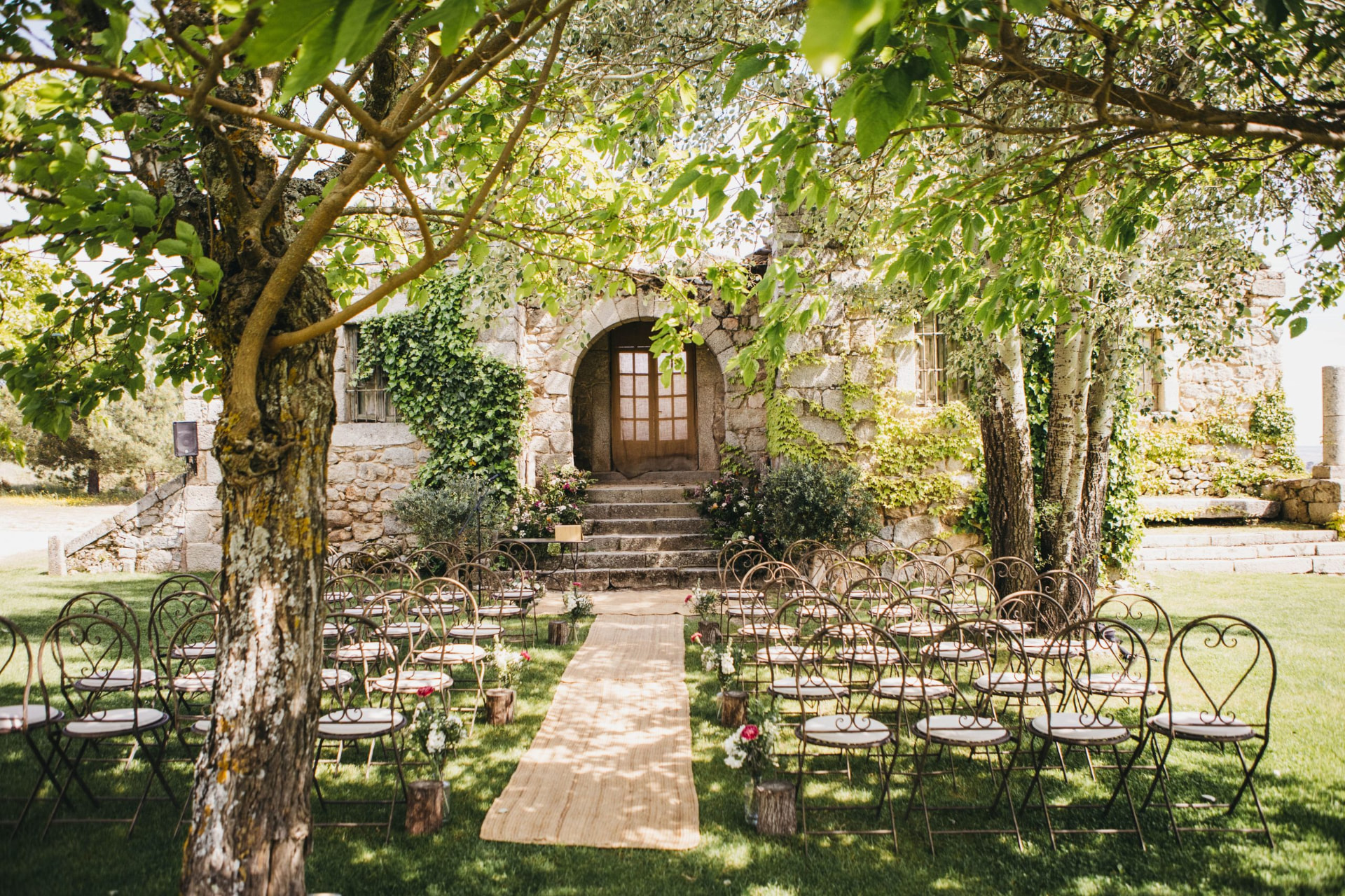 Garden ceremony set-up with iron chairs and an aisle leading to a stone arch